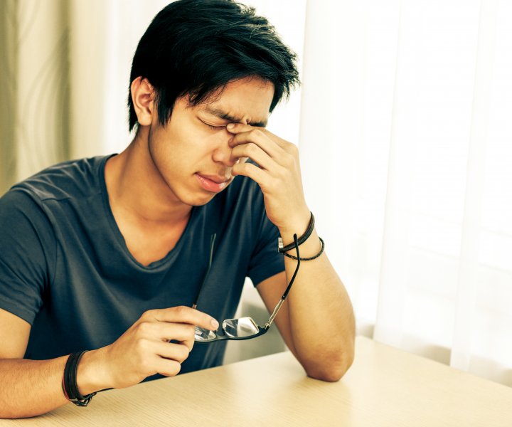Tired asian man with eye pain holding glasses in hand