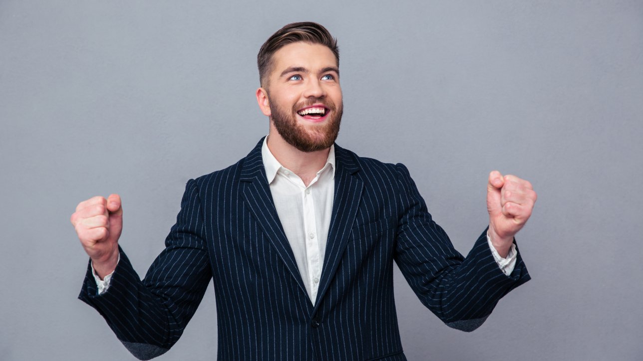 Portrait of a cheerful businessman celebrating his success over gray background