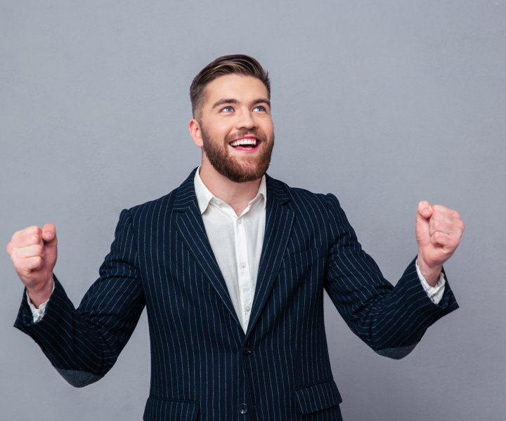 Portrait of a cheerful businessman celebrating his success over gray background