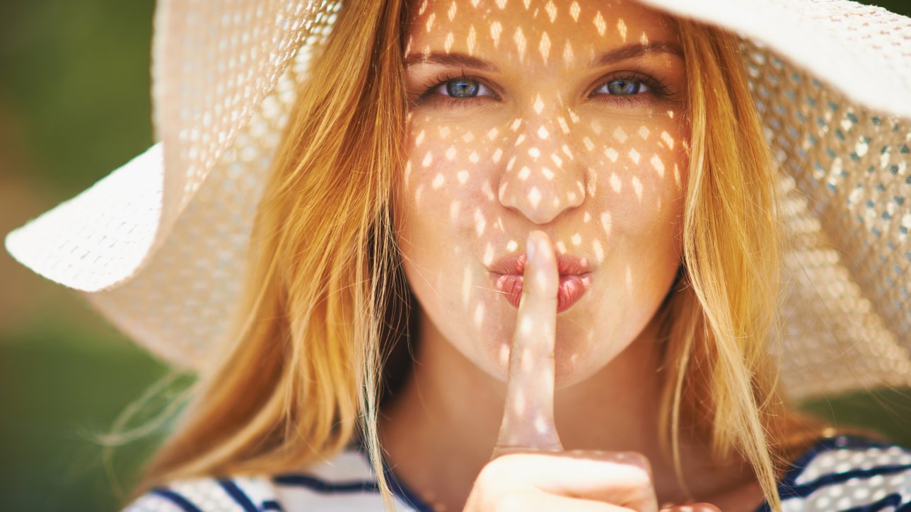 Pretty woman in sunhat looking at camera and making shh gesture